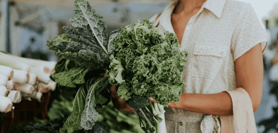 a women shopping holding a bundle of leafy greens in her hand